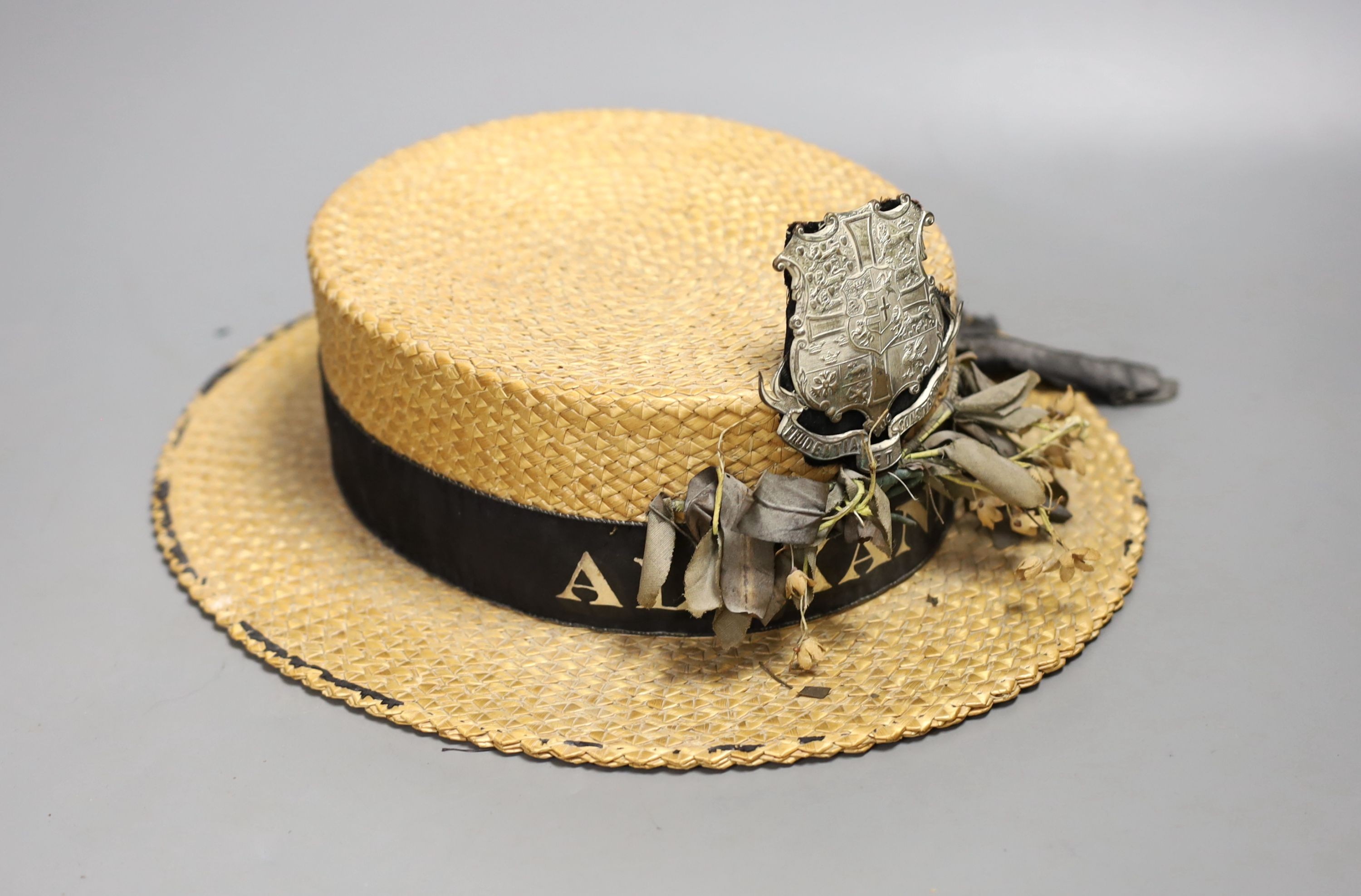 A straw boater, with crested badge and ribbon printed with ‘Alexandra’, 32 cms front to back including brim.